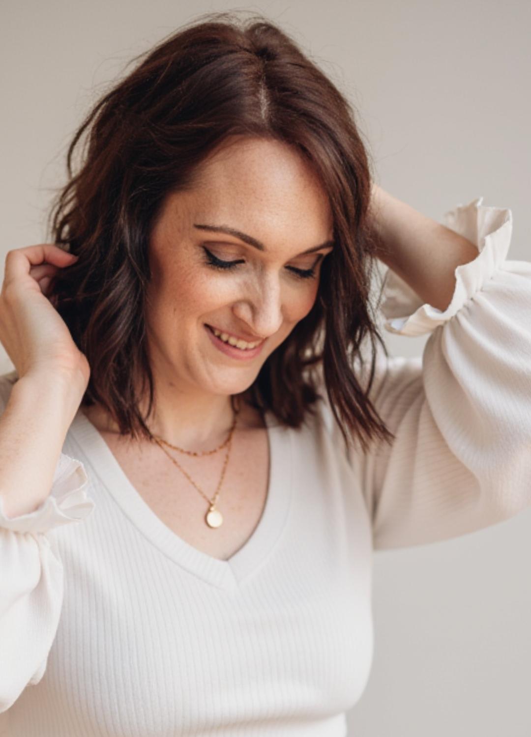 Braunhaarige Frau in weißem Pullover mit verspielten Details und Goldkette. Calico Sky Studio Webdesign & Branding Kontaktaufnahme