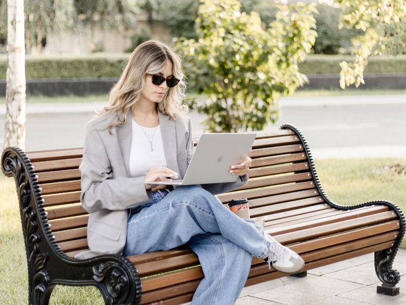 Lohnt sich Bloggen noch in 2025? 1 Blonde Frau in weiter Jeans und Blazer auf einer Parkkbank arbeitet als Fashion Blogger - lohnt sich bloggen noch