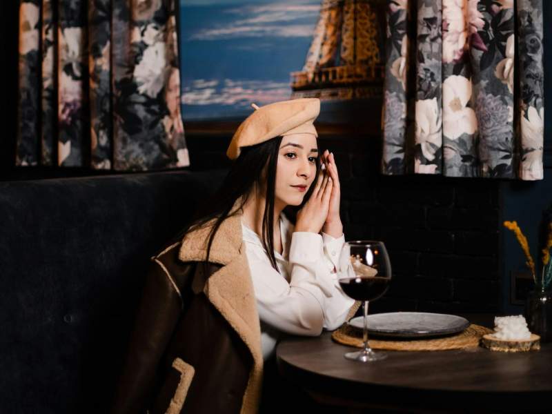 Markenpersönlichkeit entwickeln: Welche Netflix-Serie ist Deine Marke? 2 Frau in weißer Bluse und karamell-farbener Baskenmütze sitzt in Pariser Cafe. Blogartikel mit dem Thema Markenpersoenlichkeit entwickeln mithilfe von Netflix-Serie.