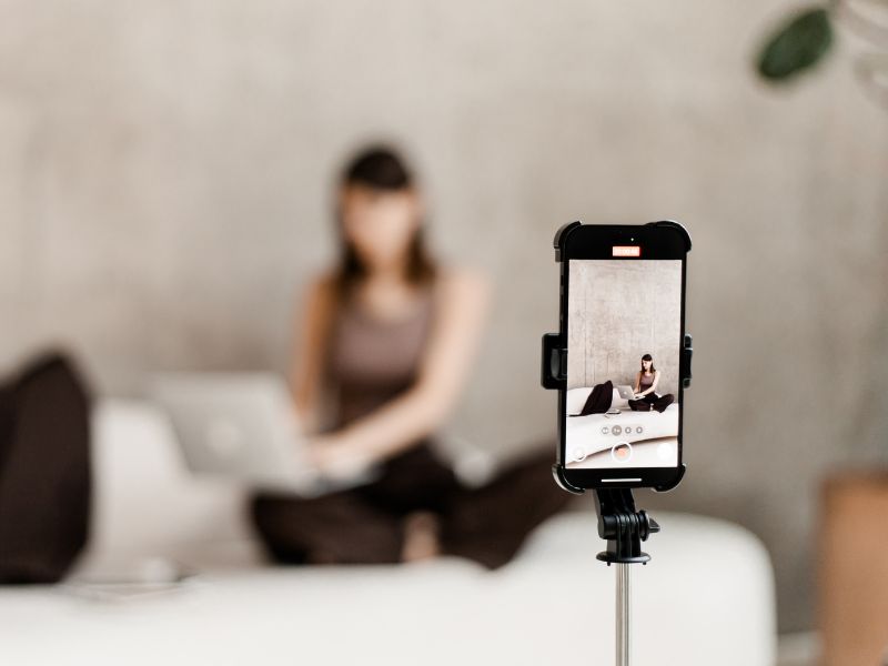Marketing ohne Druck - die 6 besten Methoden 1 Frau auf cremefarbenen Sofa in Kleidung des Farbton des Jahres Mocca Mousse. Im Vordergrund Smartphone für Social Media Content für Community-Buildung.