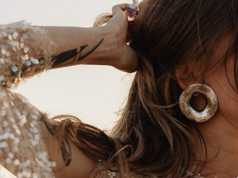 Frau mit Pailettenkleid und modischem Ohrring, die ein Tattoo am Unterarm hat. Alleinstellungsmerkmale im Personal Branding.