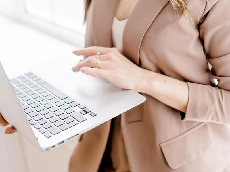 Frau in rosa pastelfarbenem Business Blazer hält Laptop. Blogartikel Webdesign-Fehler Selbstständige