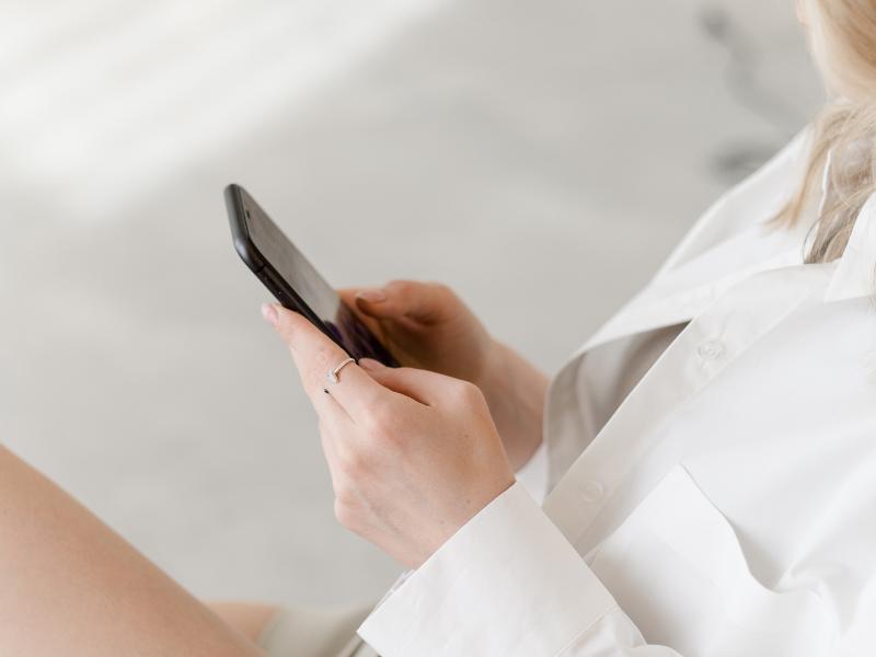 5 Webdesign-Fehler, die Selbstständige vermeiden sollten 1 Frau in weißer Bluse hält Smartphone. Foto für Blogartikel Webdesign-Fehler vermeiden, für Selbstständige. hier responsive Design beachten.