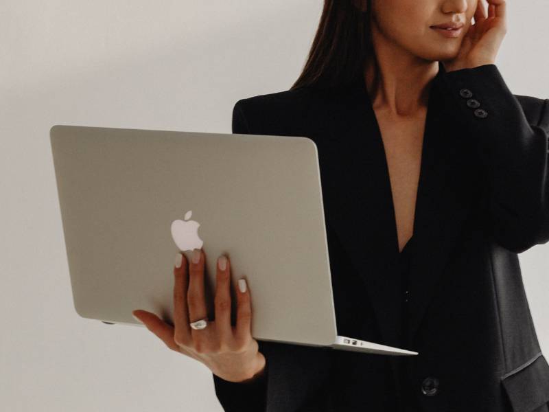 Frau im Business-Blazer hält Apple Laptop. Blogbeitrag über Lösungen für Webdesign-Anfänger für Business-Website.