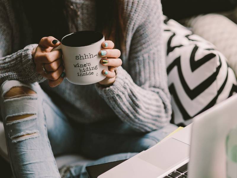 Webdesign-Anfänger? Die beste Lösung für Deine Website 1 Frau mit ripped Jeans und Kaffeetasse mit Spruch sitzt am Laptop. Website selbst erstellen oder Website Baukasten.